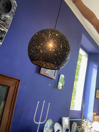 A spherical black woven pendant light with a warm glowing bulb inside, hanging in a room with a deep blue wall.