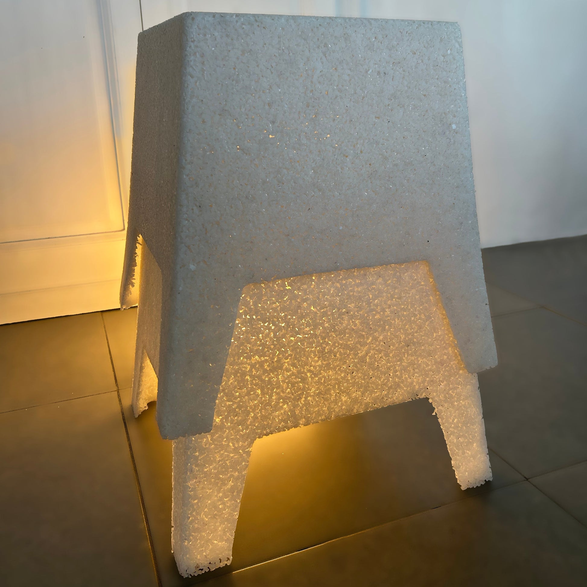 A modern, minimalist foam chair with a textured light gray outer shell and a glowing warm white illuminated base.