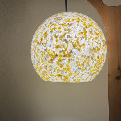 A spherical pendant light with a white and yellow plastic speckled pattern, suspended by a black cord in an indoor setting.