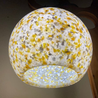 A spherical glass pendant light shade with a white base and dense yellow, gold, and gray speckled pattern, shown against a neutral indoor background.