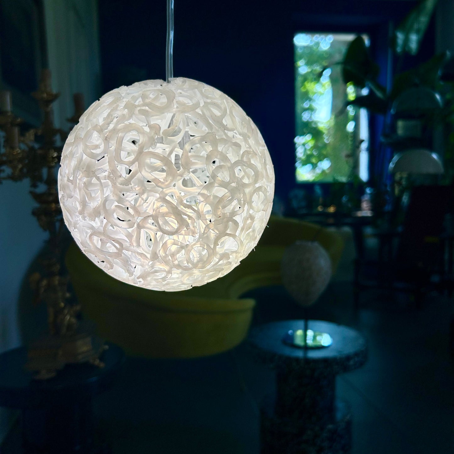 A spherical pendant light with a textured, openwork pattern glowing warm white, hanging in a dimly lit modern interior room.
