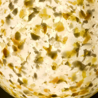 A close-up of a terrazzo plastic pattern with a warm cream base and scattered irregular flecks in beige, brown, and muted olive green.